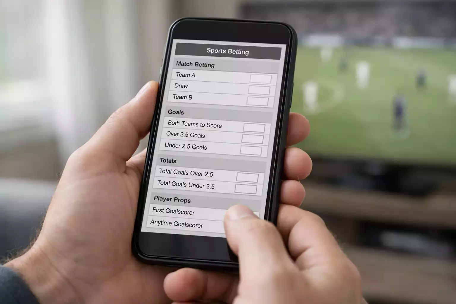 Person using betting app on smartphone with football match playing on TV in background