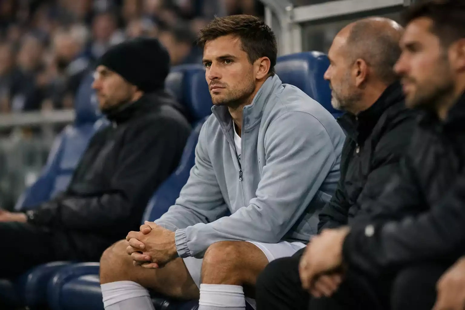 Football player sitting on the bench wrapped in a training jacket watching the match