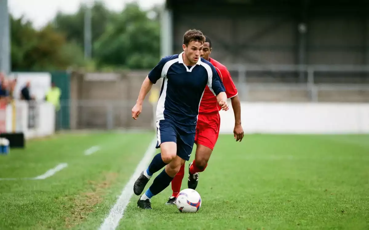 Football winger running with the ball down the sideline toward the corner flag