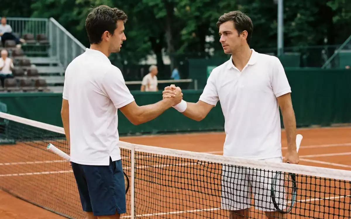 Two tennis players shaking hands at the net after completing a competitive match